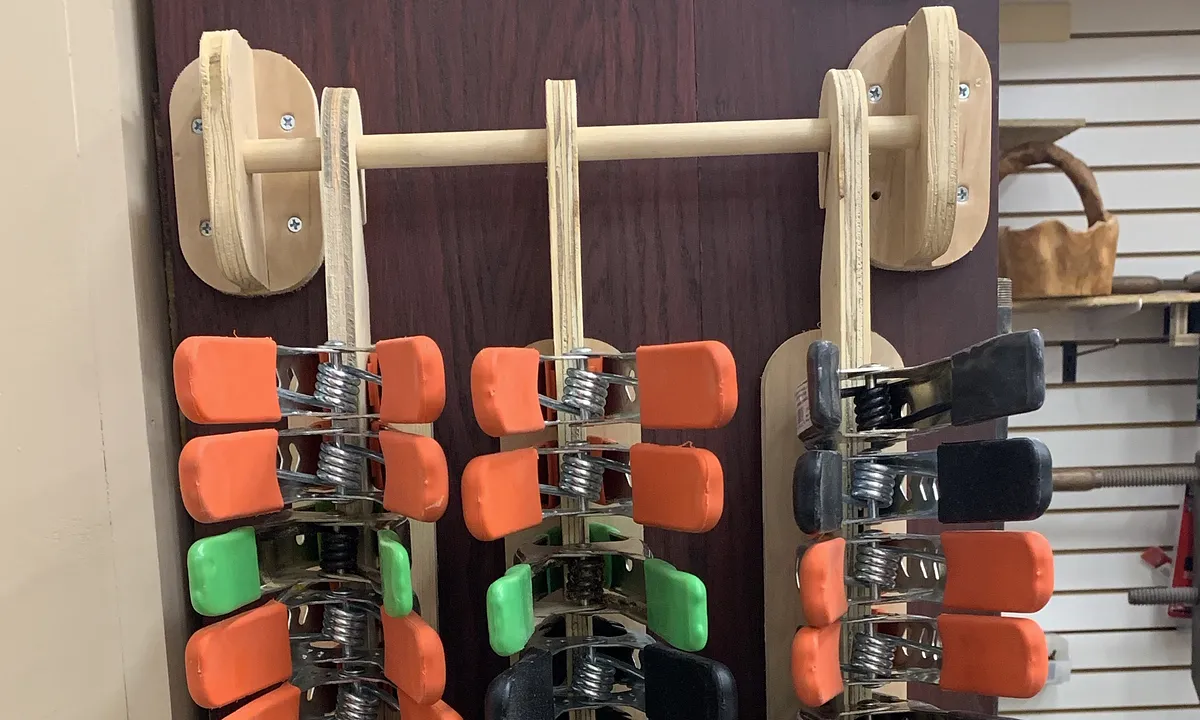 Wall-mounted plywood rack holding orange and green spring clamps