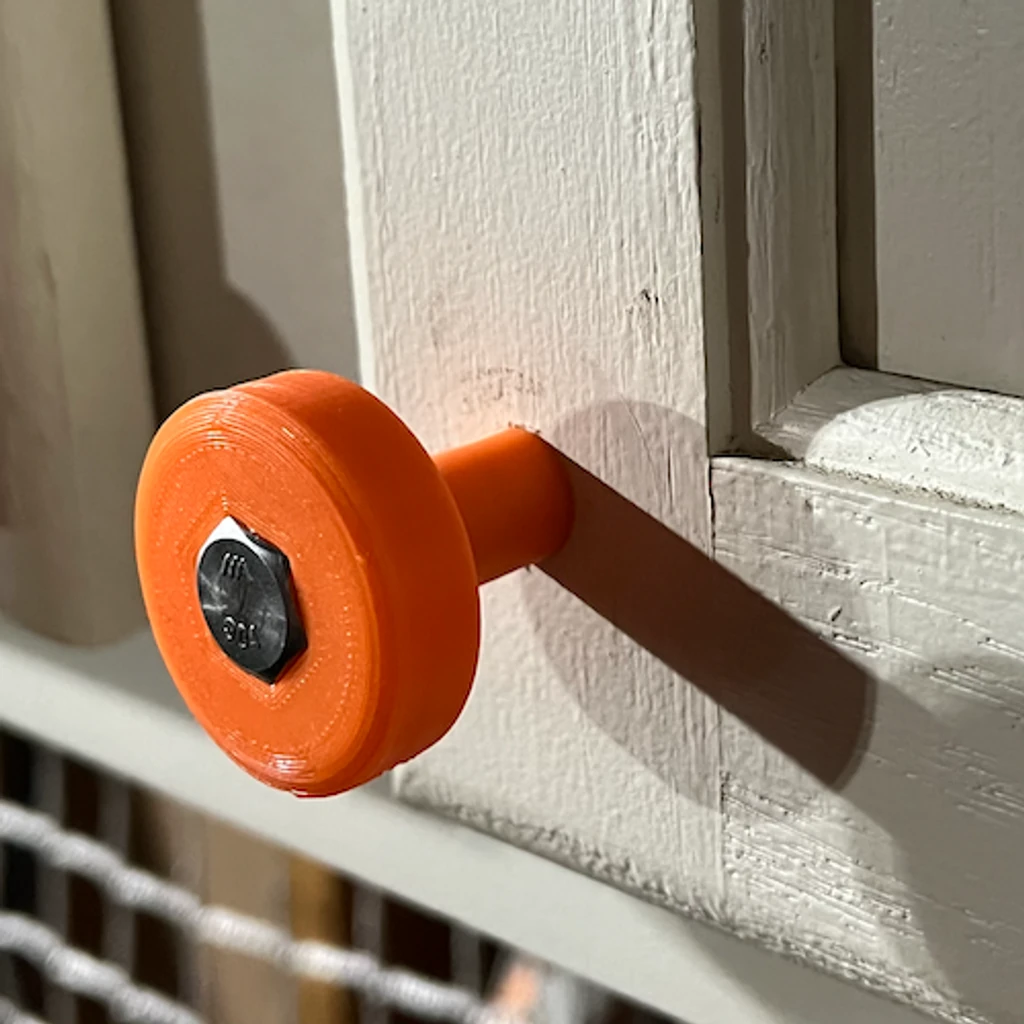 Orange printed cabinet knob fastened with a bolt on a painted cabinet door
