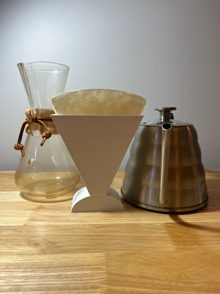 Printed holder keeping folded coffee filters together beside a Chemex