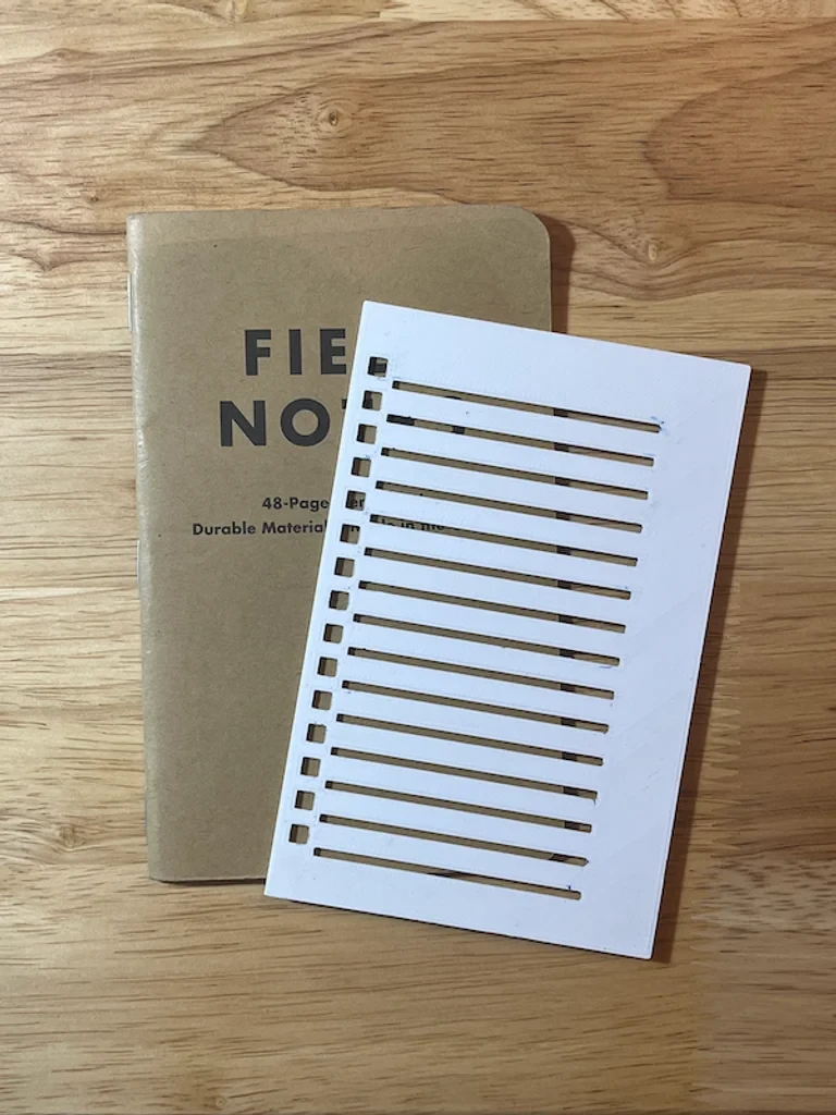 White printed checklist stencil resting on a Field Notes notebook on a wooden table