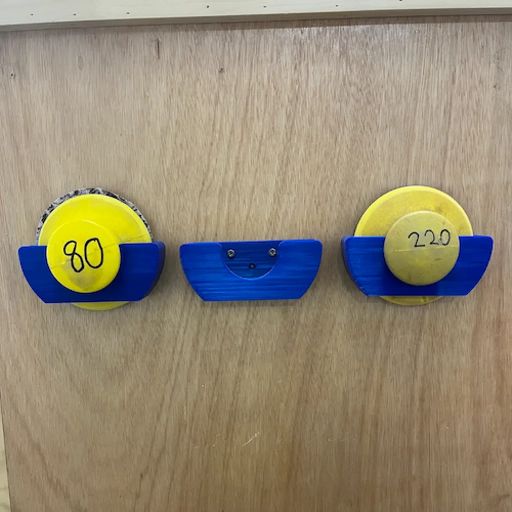 Three blue printed sanding pad holders mounted on a wooden wall, two holding yellow pads